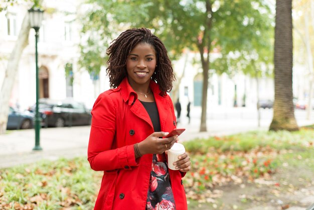 Woman with smartphone and paper cup smiling