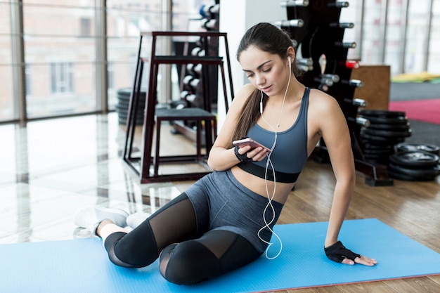 ジムに座っているスマートフォンを持つ女性