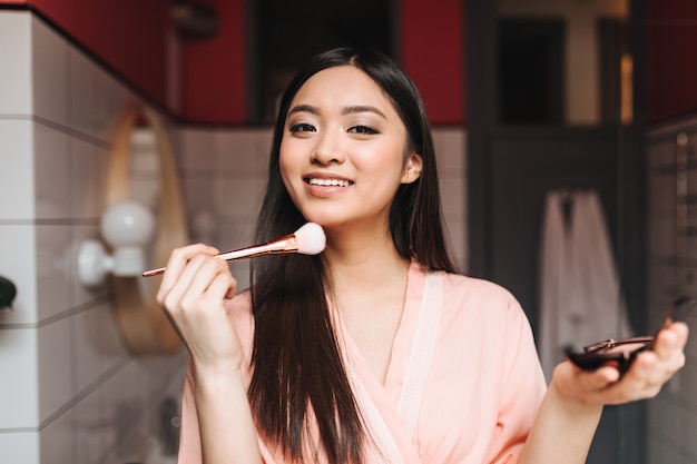 Woman with smile looks into front and puts powder on her face with brush