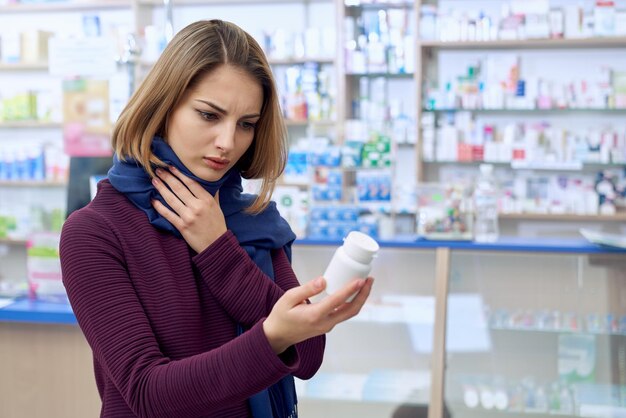 Woman with sore throat choosing pills in drugstore