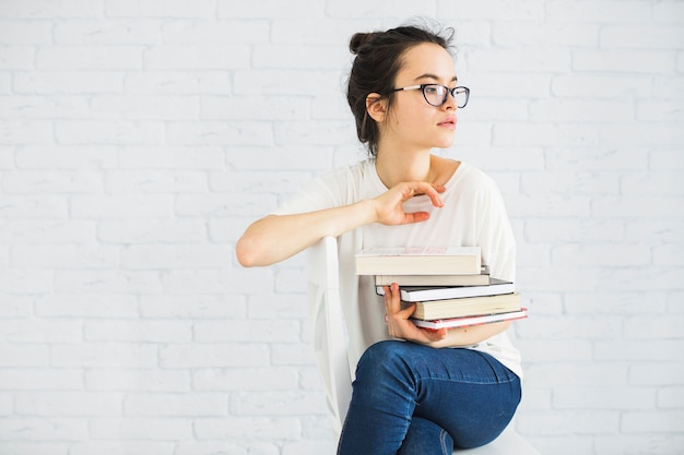 Foto gratuita donna con una pila di libri sulla sedia