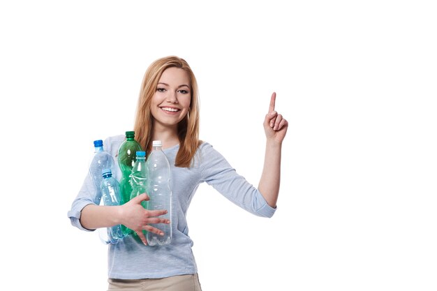 Woman with stack of plastic bottles pointing at copy space