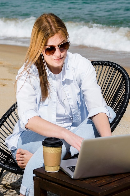 선글라스와 해변에서 일하는 노트북을 가진 여자