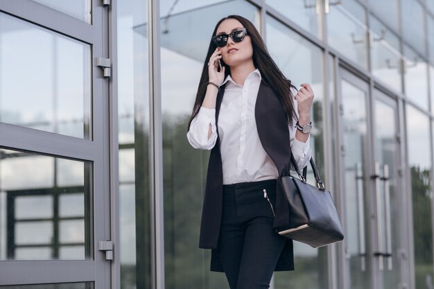Woman with sunglasses talking on the phone with giant windows behind