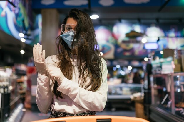 Woman with the surgical mask and the gloves is shopping in the supermarket