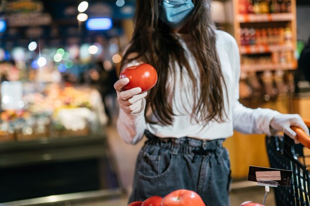 수술 용 마스크를 가진 여자는 토마토를 구입할 것입니다.