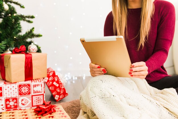 Woman with tablet near gift boxes and Christmas tree
