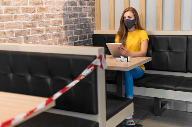 Foto gratuita donna con la maschera d'uso della compressa che rispetta le nuove misure al terrazzo