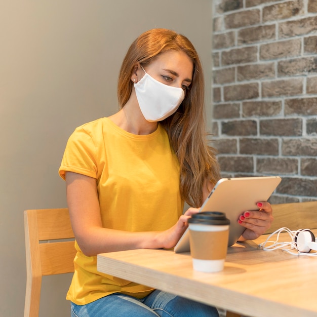 Free photo woman with tablet wearing mask