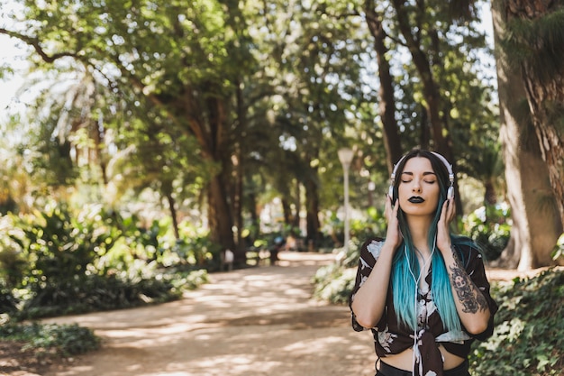 Woman with tattoo in her hand enjoying music on headphone standing in the park