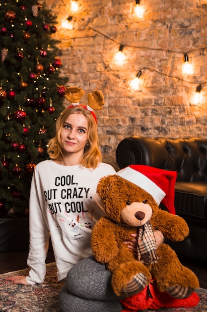 Woman with teddy bear sitting next to christmas tree