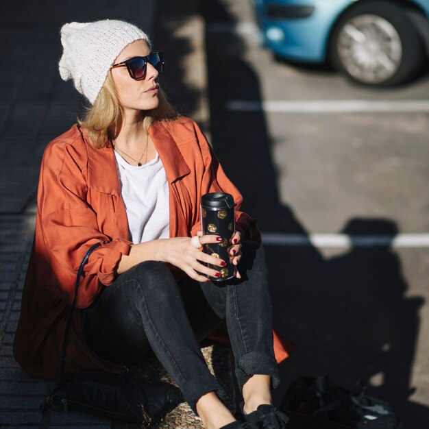 Женщина с термос, сидя на тротуаре