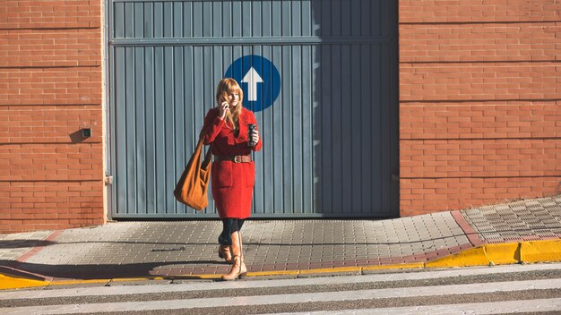 Woman with thermos and smartphone crossing street