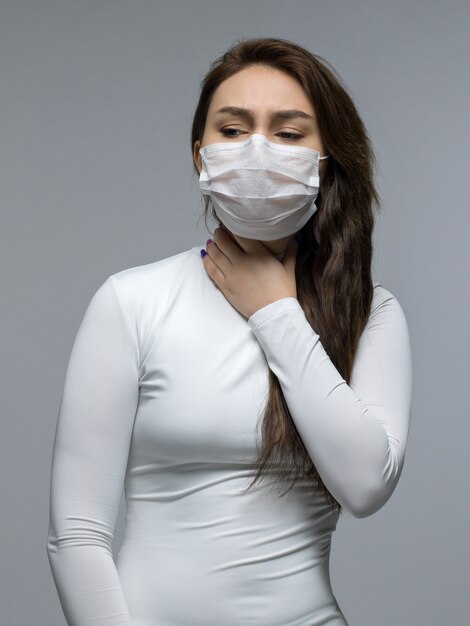 Woman with throat problems holding it in white protective mask