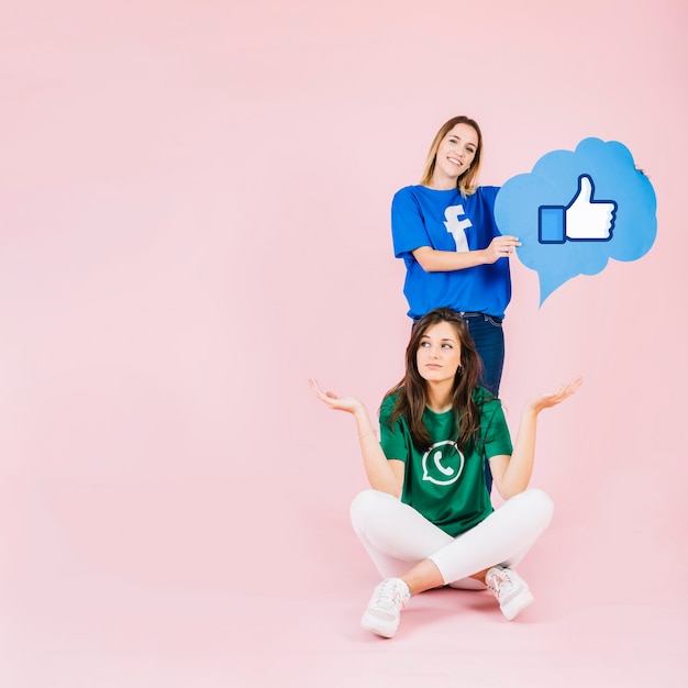 Woman with thumbs up sign speech bubble behind her friend shrugging