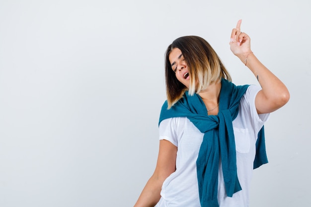 Woman with tied sweater posing while pointing up in white t-shirt and looking energetic. front view.