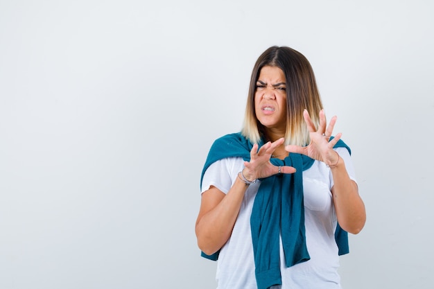 Woman with tied sweater showing stop gesture in white t-shirt and looking disgusted. front view.
