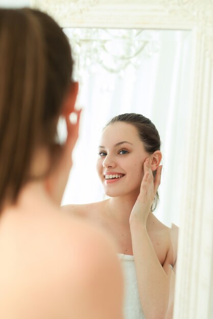 Woman with towel on body after shower, looking in mirror