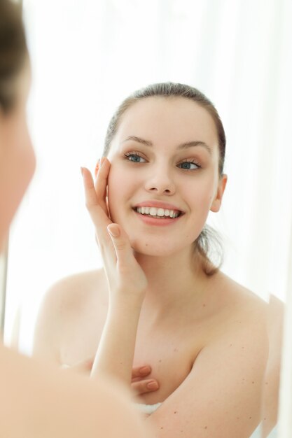 Woman with towel on body after shower, looking in mirror