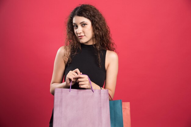 Woman with tricky glance holding many of bags on red
