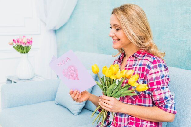 Женщина с тюльпанами на диване читает открытку