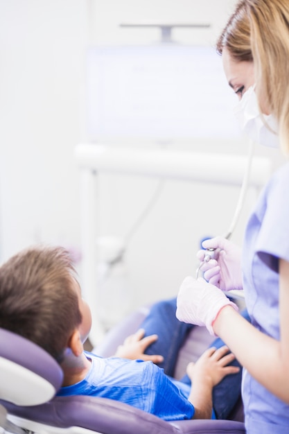 Женщина с ультразвуковой скалер, стоя рядом с мальчиком, сидя на стоматологическом стуле