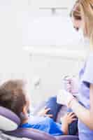 Бесплатное фото Женщина с ультразвуковой скалер, стоя рядом с мальчиком, сидя на стоматологическом стуле