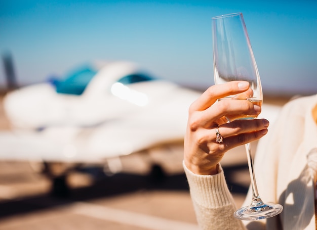 Woman with wedding ring holds glass of champagne standing in the airport