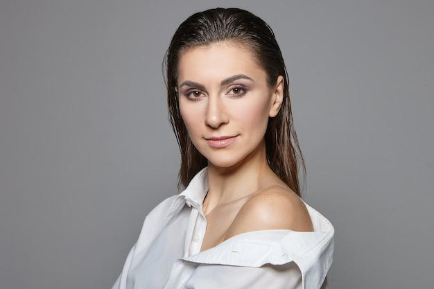 Woman with wet dark hair combed back wearing silk oversize shirt with one shoulder nude.