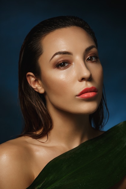 Free photo woman with wet hair and face covering body with leaf.