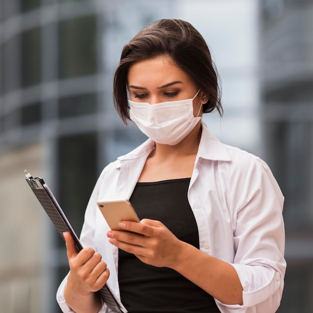 Woman at work outdoors with smartphone and notepad during pandemic