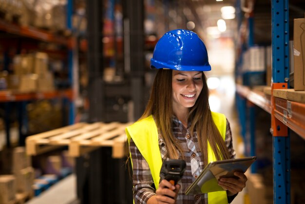 Woman worker holding tablet and bar code scanner checking inventory in large distribution warehouse