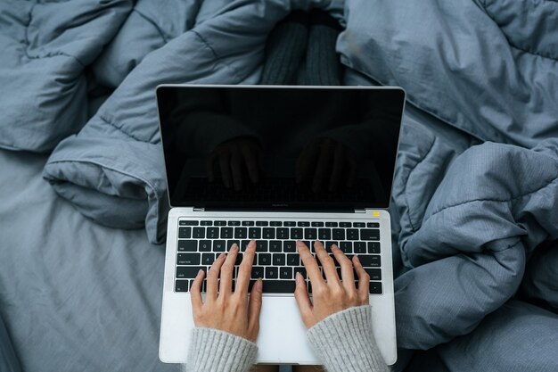 Woman working on laptop on her bed in cold day