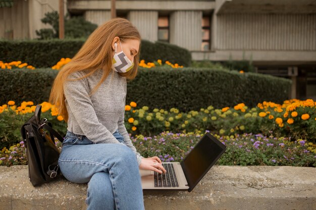 医療用マスクを着用しながら屋外でノートパソコンで作業する女性