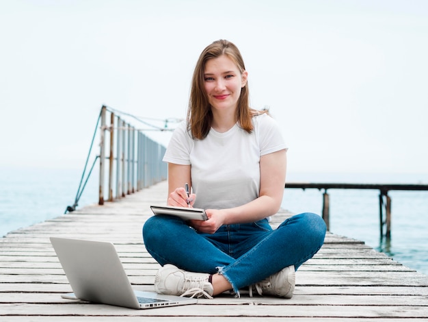 Foto gratuita donna che lavora al computer portatile fuori sul molo