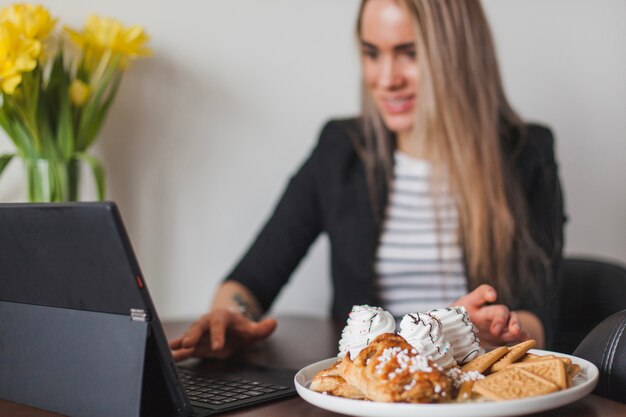 Woman working on laptop with pastry in foreground