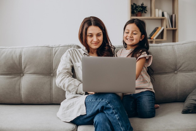 Woman working online on laptop at home with daughter