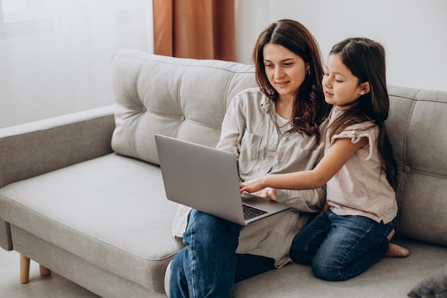 Женщина работает онлайн на ноутбуке дома с дочерью