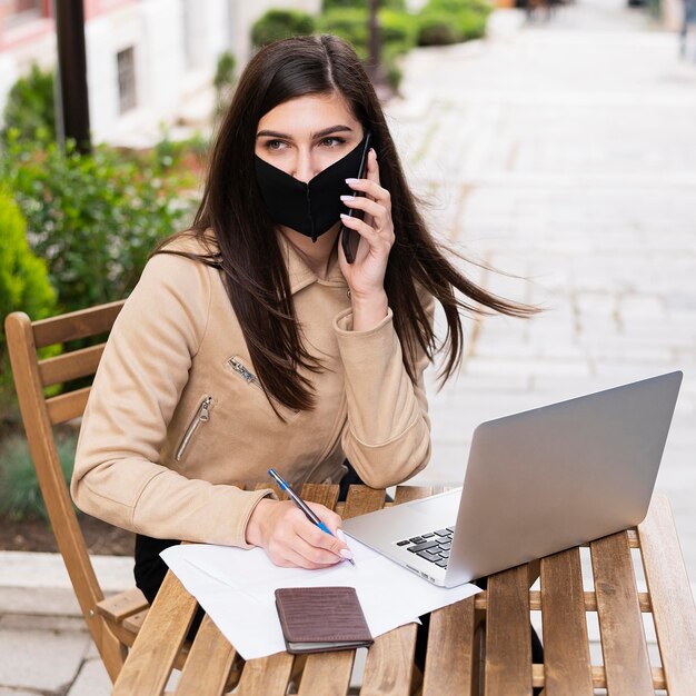 Женщина работает на открытом воздухе на ноутбуке с лицевой маской