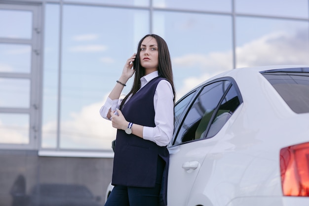Woman would be talking on the phone leaning on a car