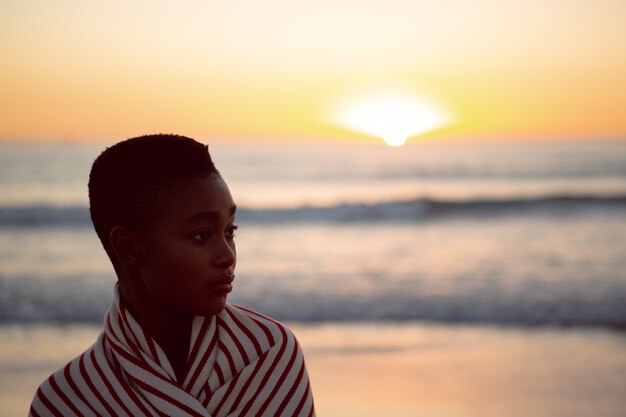 Woman wrapped in blanket standing on the beach