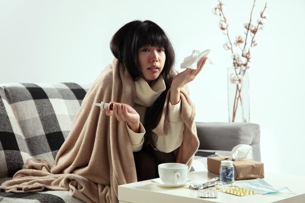 Woman wrapped in a plaid and wearing face mask trying to protect herself from somebody's sick