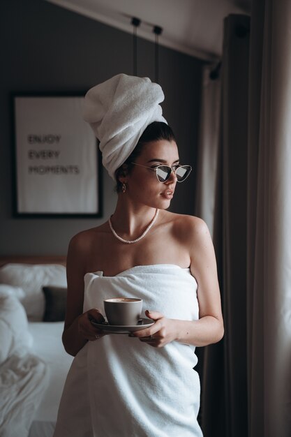 Женщина, завернутая в полотенце, пьет кофе