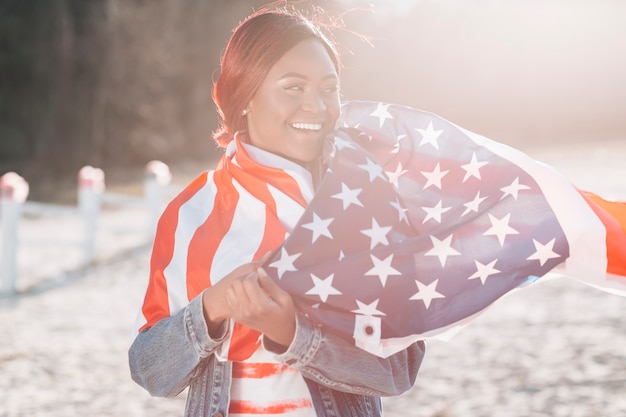 Foto gratuita donna avvolta nella bandiera usa in piedi sulla sabbia