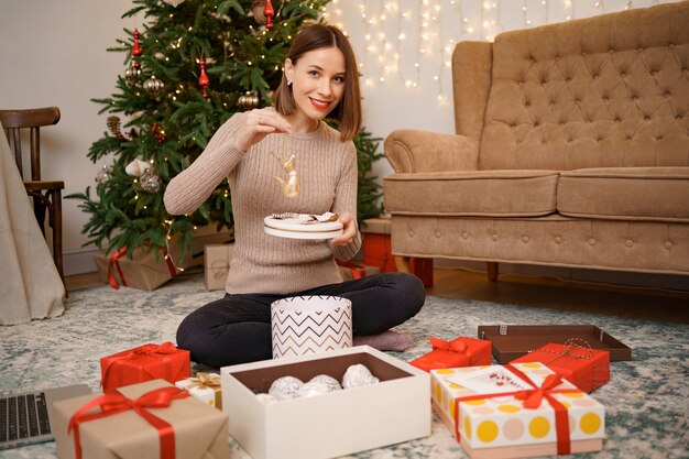 Woman wrapping Christmas gift while sitting on the carped in the living room