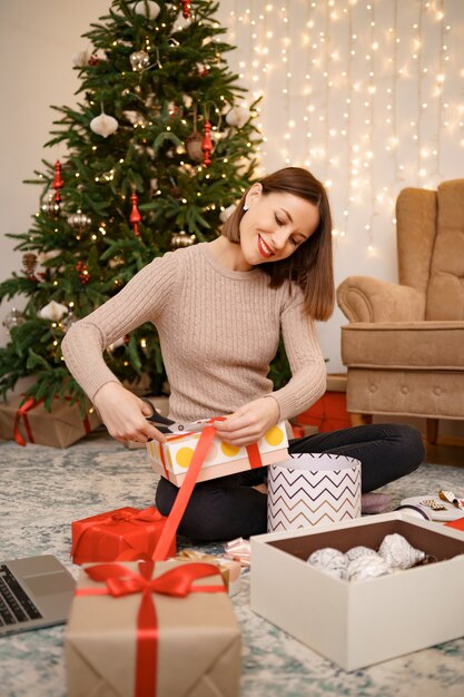 Woman wrapping Christmas gift while sitting on the carped in the living room