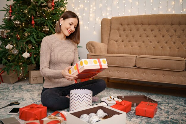 Woman wrapping Christmas gift while sitting on the carped in the living room