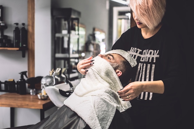 Woman wrapping customer in towels in barbershop