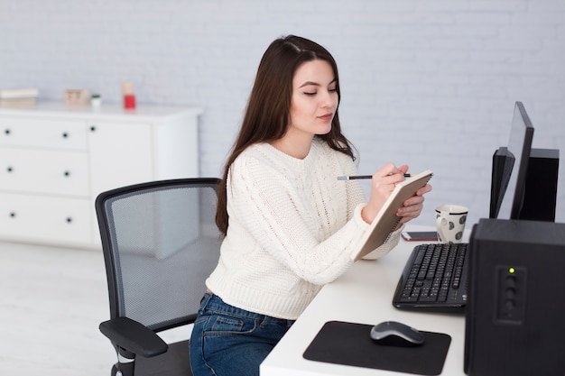 Woman writing in notepad at computer