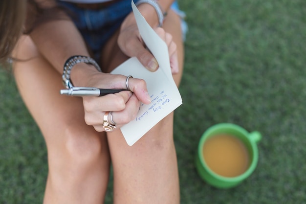 Woman writing with pen on white paper with cup of coffee